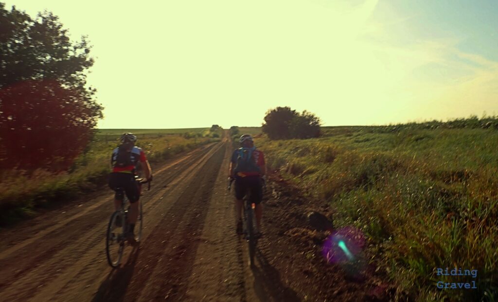 Two riders on a dirt road cycling.